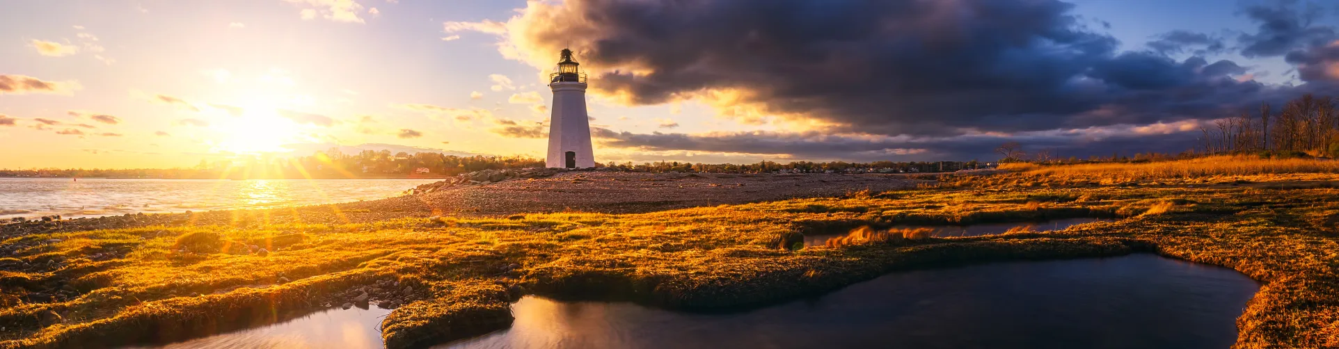 A sunset scene of a lighthouse on a rocky shore
