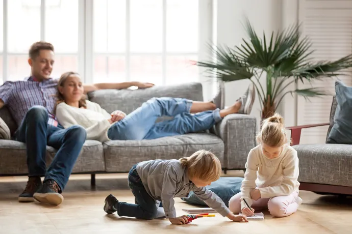 Parents lounging on a couch while they watch two children play in the living room