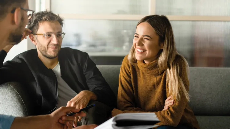 A young couple sitting on a couch, smiling and engaging in a conversation with a financial advisor
