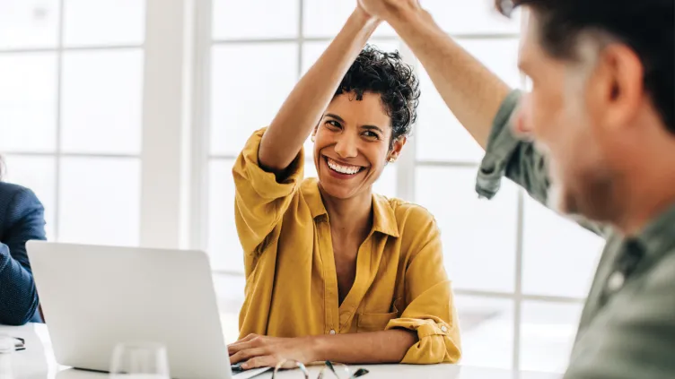 Two colleagues high-fiving in an office setting, smiling and celebrating a success