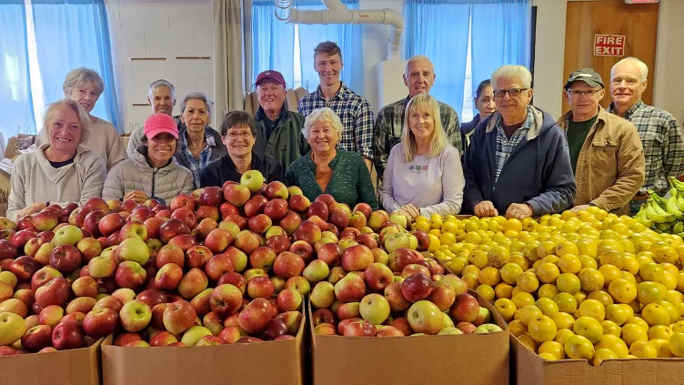 Group standing in front of card board boxes with many apples