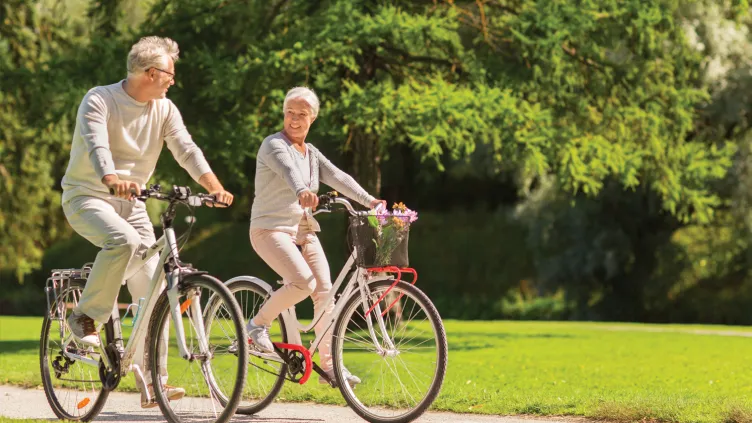 An elderly couple happily riding bicycles in a park on a sunny day