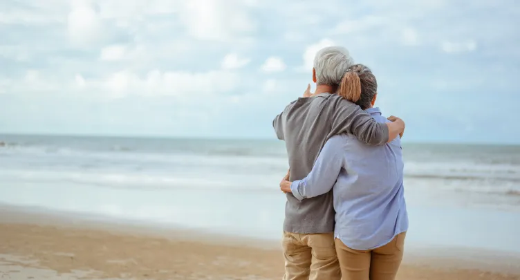 A couple stands on a beach, looking at the ocean
