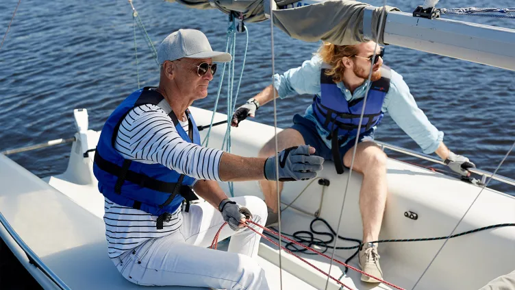 Father and son wearing life jackets holding ropes while handling sailboat together