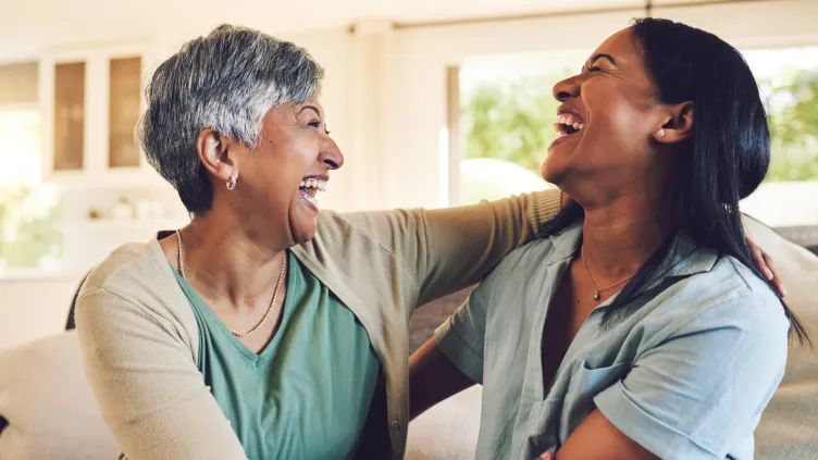 Two women of different generations laughing heartily together in a living room